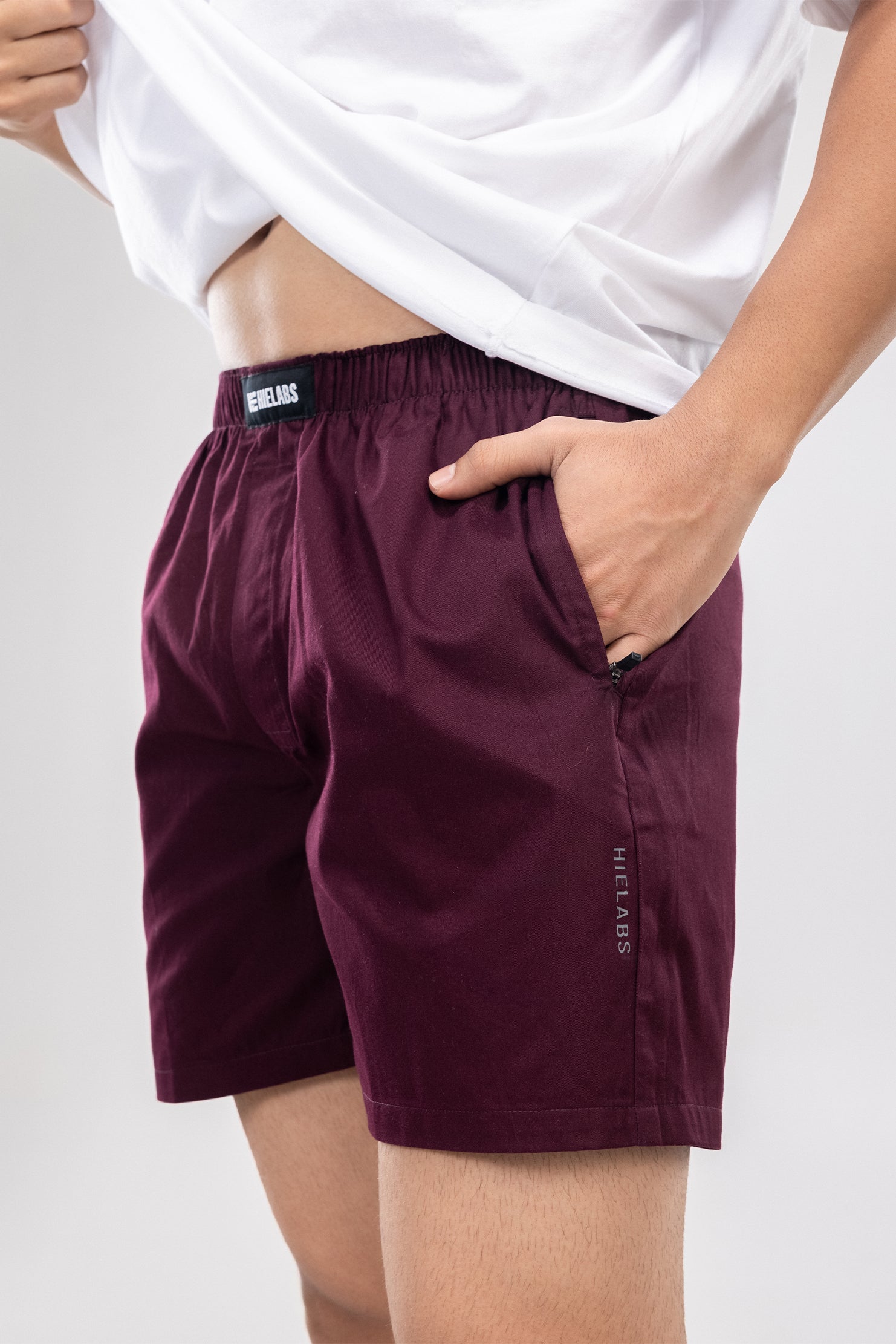 Person wearing a white t-shirt and maroon HIELABS boxers with an elastic waistband, hand in pocket.